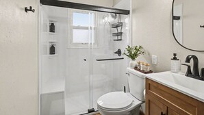 Een moderne badkamer met een douchecabine van glas, een wit toilet, een wastafel met een zwarte kraan en een spiegel boven de wastafel.