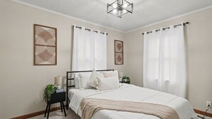 Een slaapkamer met een groot bed, twee nachtkastjes, een bijzetmeubel en een plafondlamp.