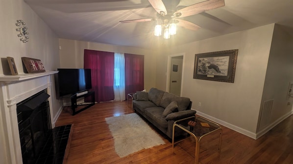 A living room with a fireplace, a television, a sofa, and a ceiling fan.