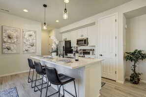 Une cuisine moderne avec des meubles blancs, un grand îlot central doté de tabourets, des appareils en acier inoxydable et des œuvres d’art florales décoratives.