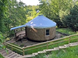 Una yurt con un terrazza in legno e un piccolo oblò, immersa in una foresta.