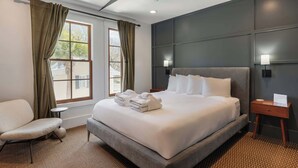 Hotellihuone, jossa on suuri sänky, tuoli, pieni pöytä ja yöpöytä.