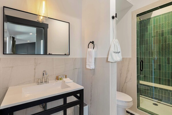 A bathroom with a white sink, a mirror, a towel rack, and a green-tiled shower enclosure.