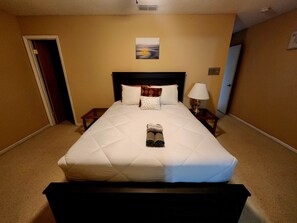 A hotel room with a large bed, a bedside table with a lamp, a door, and a painting on the wall. - Spacious 4-bedroom house with AC in Palm Coast with only 15 minutes to the Beach (Palm Coast)