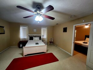 Ein Schlafzimmer mit Bett, Deckenventilator, Nachttisch, Stuhl und einem roten Teppich.