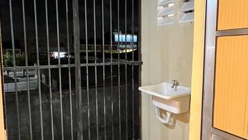 A room with a tiled floor, a white sink, a wooden door, and a barred entrance.