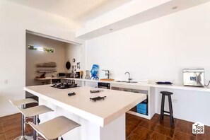 A modern kitchen with a central island, bar stools, a sink, and a refrigerator.