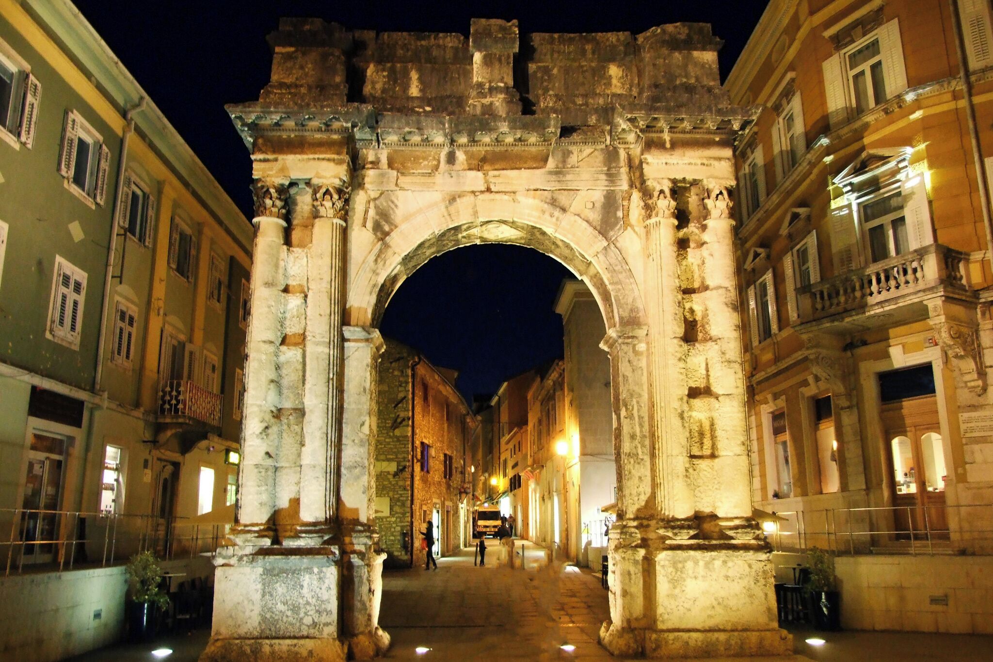 Un’antica arcata in pietra con colonne, affiancata da edifici con balconi e finestre.