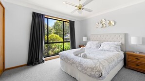 A bedroom with a large bed, a nightstand, a ceiling fan, and a window with curtains. - The Bay House - Fireplace - Waterfront (Callala Bay)