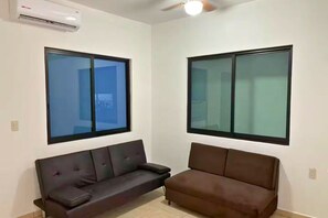A room with two sofas, a ceiling fan, and large windows.