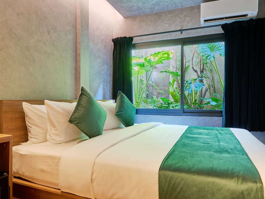 Una habitación de hotel con cama, mesita de noche, ventana con cortinas y un equipo de aire acondicionado.