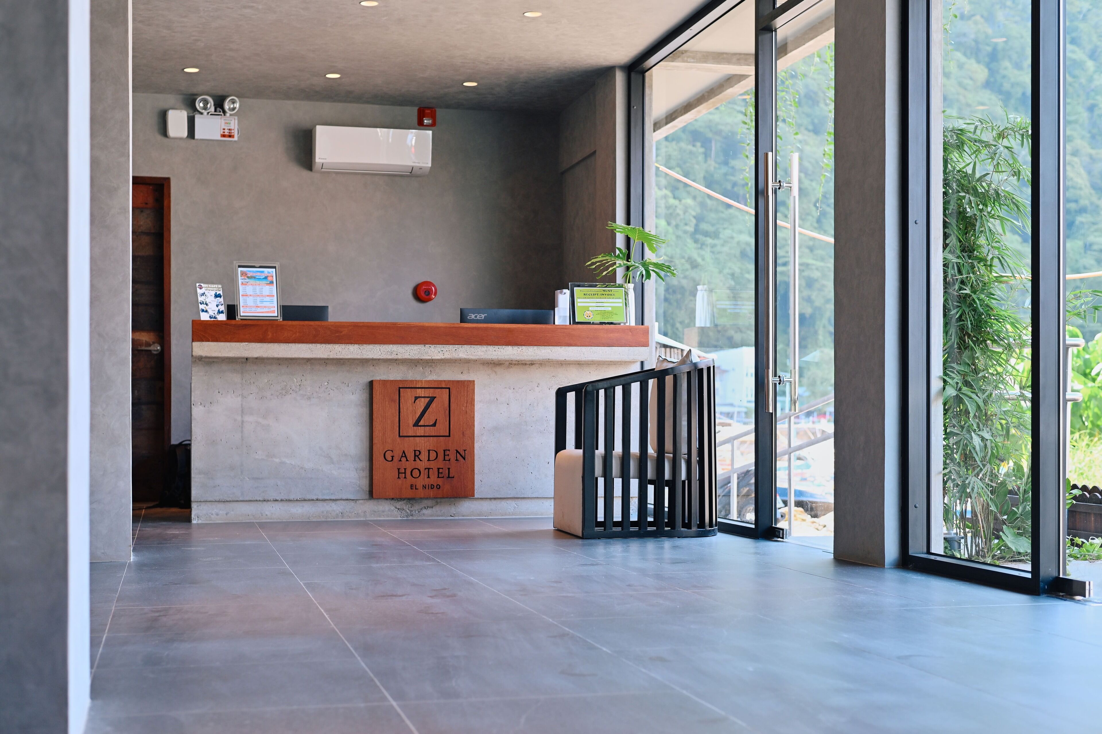 A reception area with a wooden counter, a sign for 'Garden Hotel El Hondo,' and a view of greenery outside.