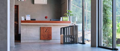 A reception area with a wooden counter, a sign for 'Garden Hotel El Hondo,' and a view of greenery outside.