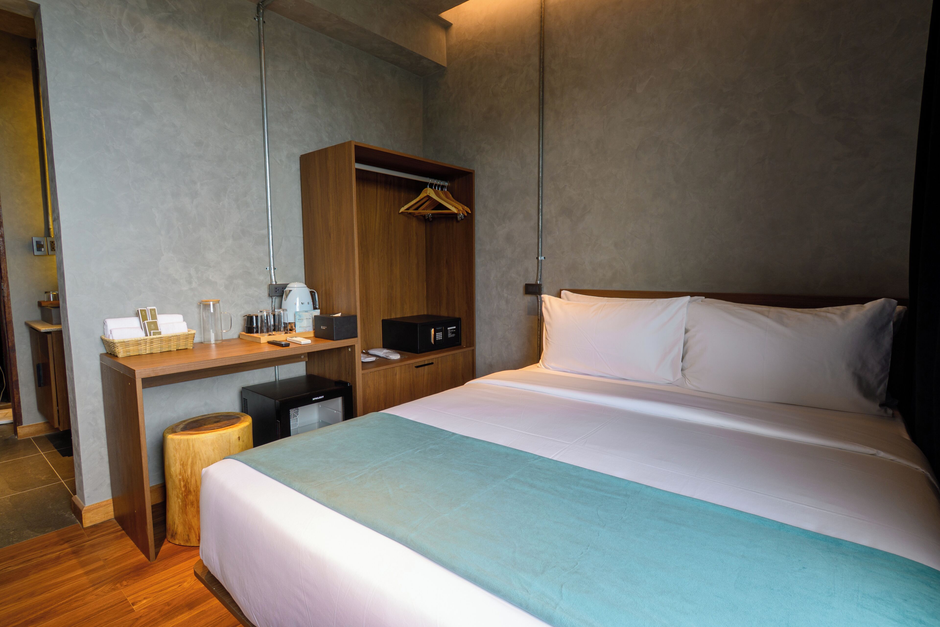 Una habitación de hotel con cama, un escritorio con computadora, un armario y un pequeño taburete.