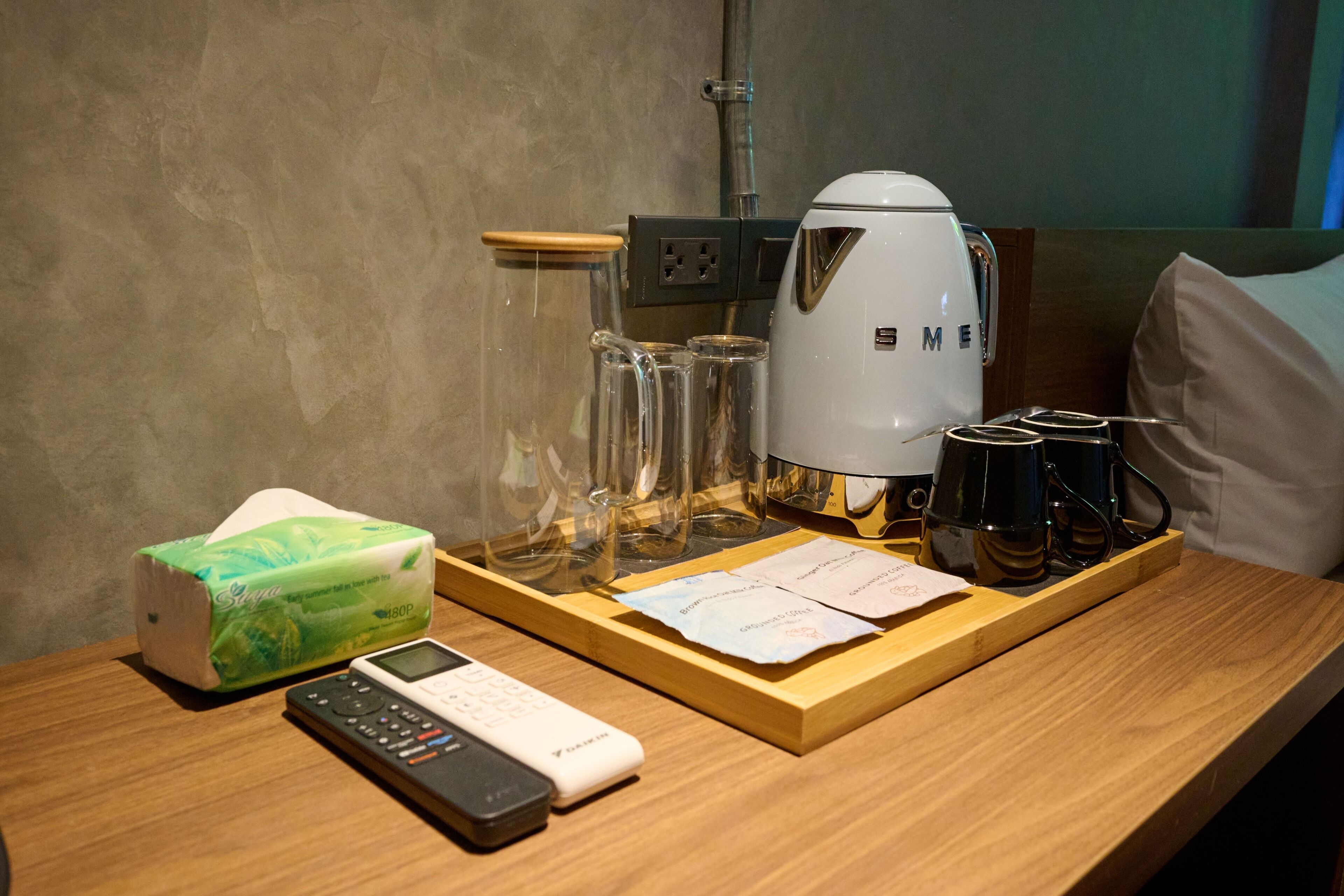 Habitació d'hotel amb escriptori de fusta, cafetera blanca, comandament a distància, caixa de mocadors i safata amb vasos i menú.