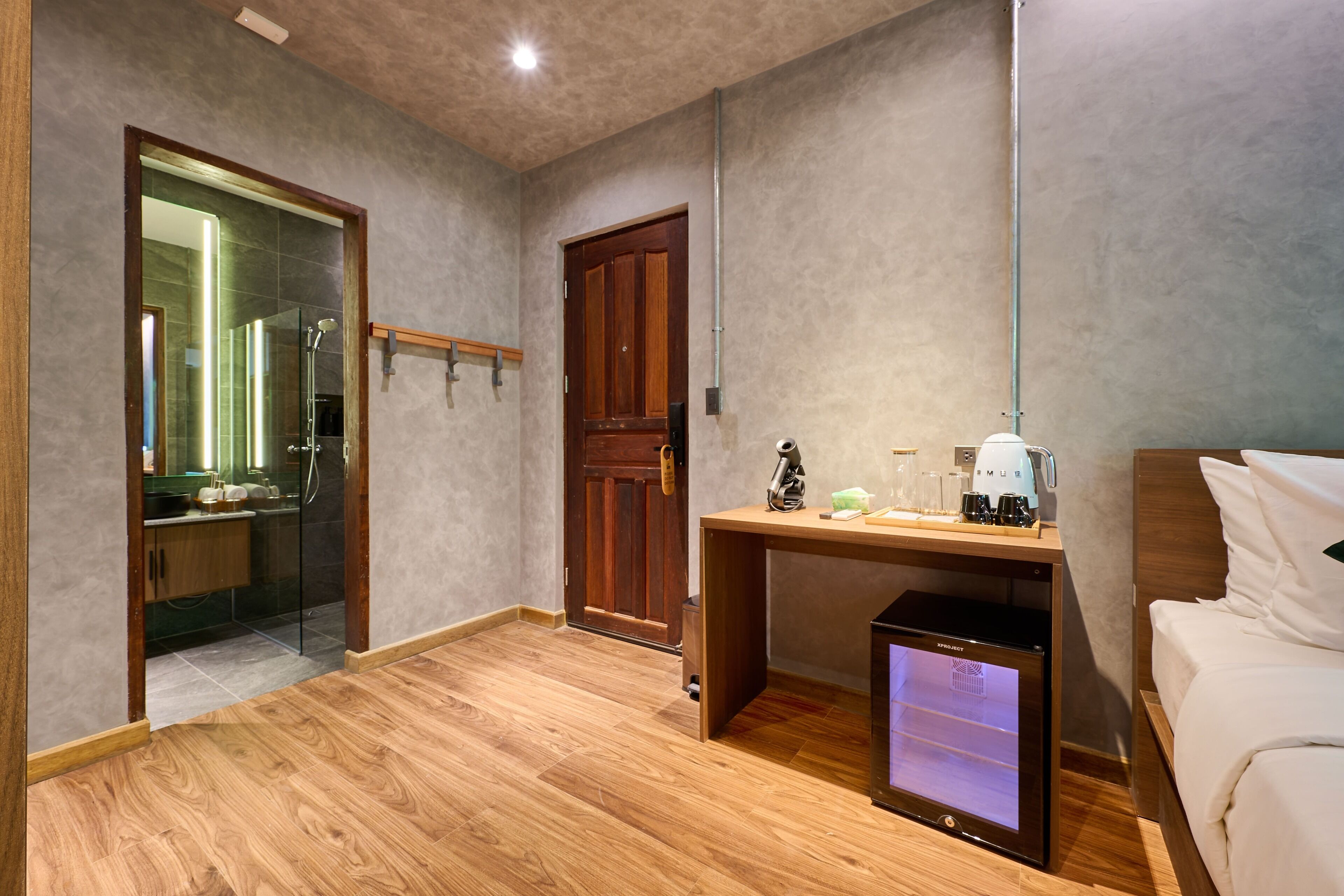 A hotel room with a wooden floor, a desk with a coffee maker, a TV, and a bed.