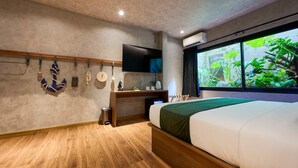 Ein modernes Hotelzimmer mit einem großen Bett, einem Schreibtisch mit Flachbildfernseher, einer kleinen Mülltonne und einem Fenster mit Blick auf Grünflächen.
