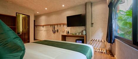 Una camera d'albergo con un letto, una TV, una scrivania in legno e una finestra vista verde.