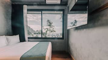 A bedroom with a large window, a bed, and a view of a landscape.