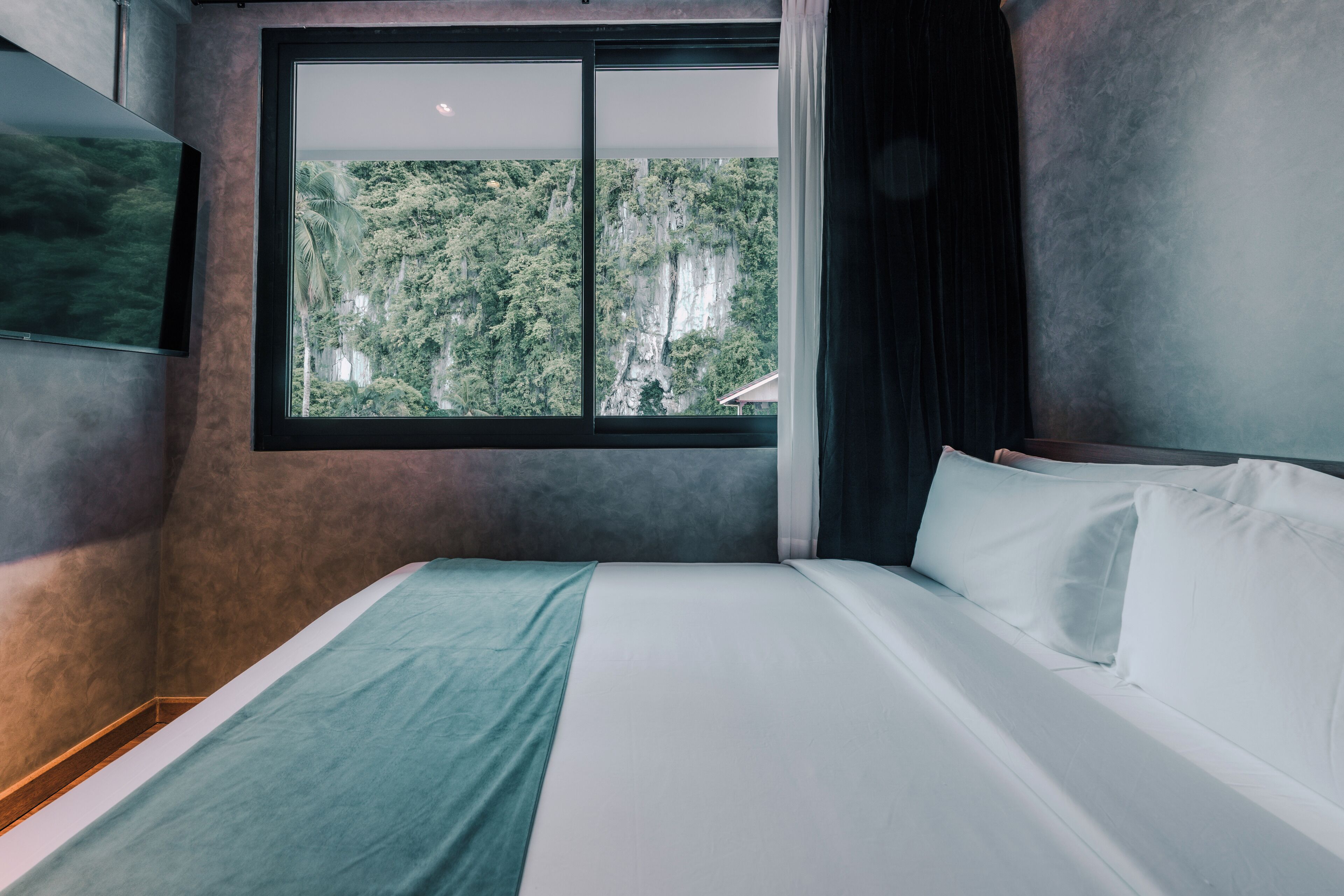 Un dormitorio con un gran ventanal, una cama y un televisor montado en la pared.