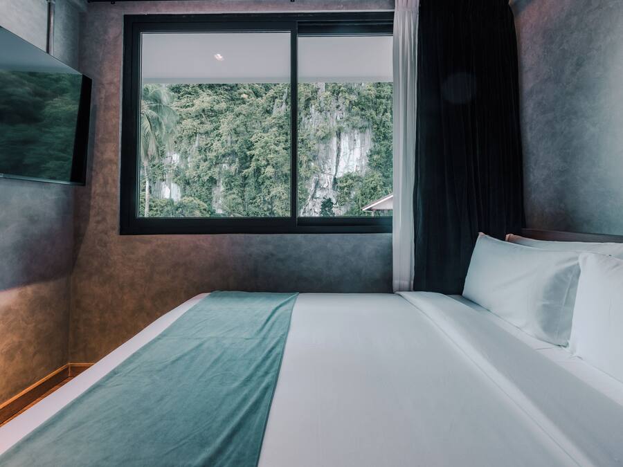 Un dormitorio con un gran ventanal, una cama y un televisor montado en la pared.