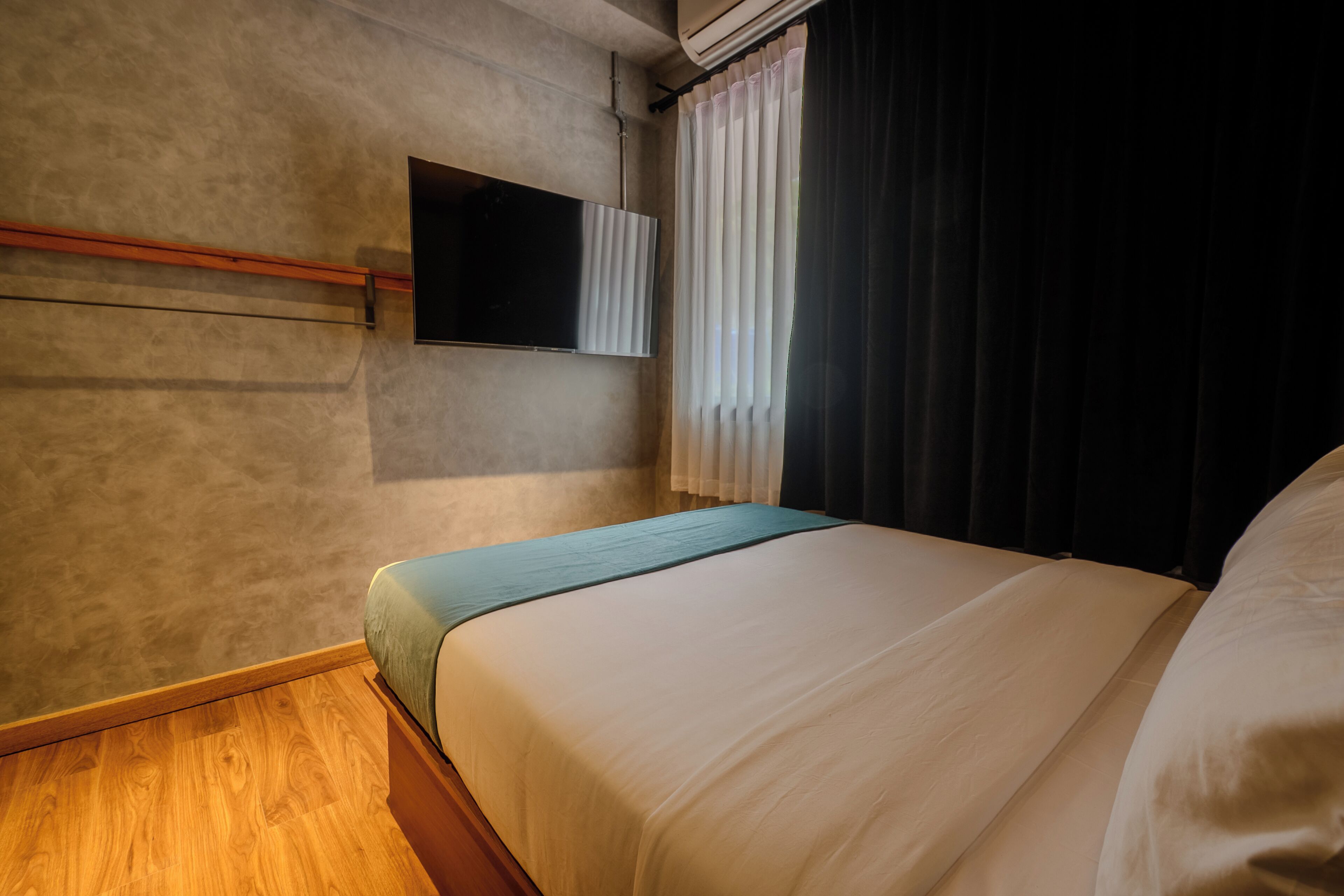 Ein Hotelzimmer mit Bett, Flachbildfernseher an der Wand und einem Vorhangfenster.