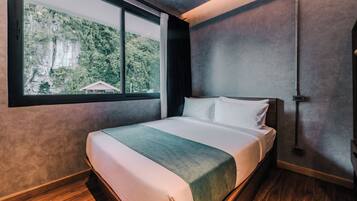 A modern hotel room with a large bed, a window with a view of greenery, and a wooden floor.
