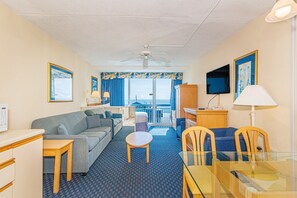 A hotel room with a sofa, a small table, a glass dining table, a TV, and a balcony with a view. - Yachtsman S504 Studio (Myrtle Beach)