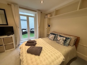 Ein Schlafzimmer mit Bett, Fernseher, einem Fenster mit Vorhängen und Blick ins Freie.
