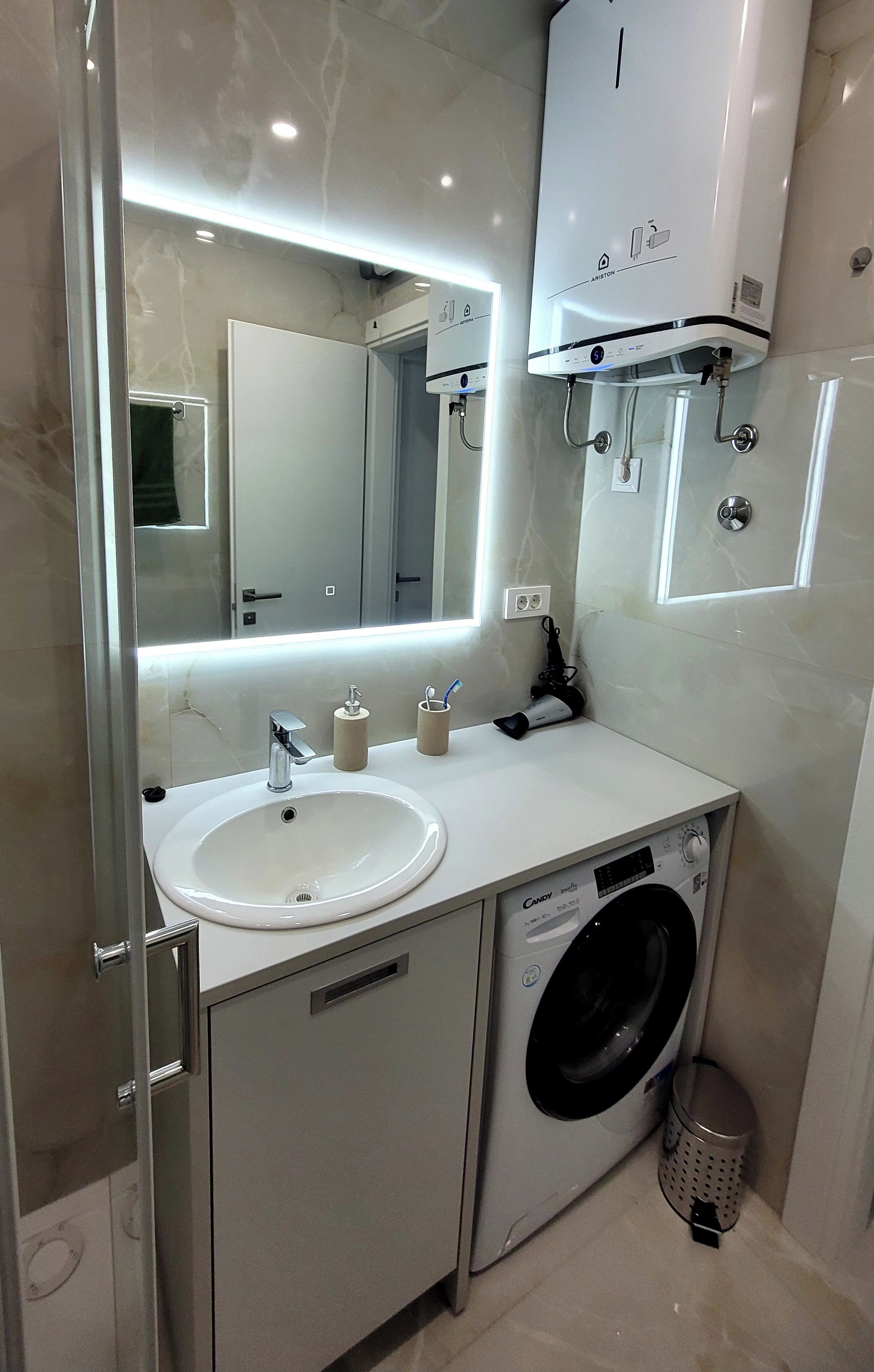 Une salle de bain moderne équipée d’un lavabo, d’un miroir et d’un lave-linge encastré.