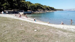 Een strand met mensen die zonnebaden en zwemmen, omringd door bomen en een heldere lucht.