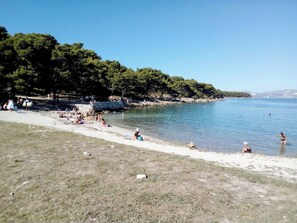Ein Strand mit badenden und sonnenden Personen, umgeben von Bäumen und einem klaren Himmel.