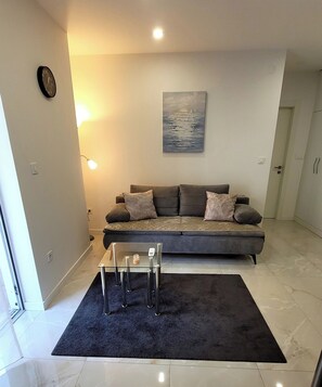 Ein modernes Wohnzimmer mit einem grauen Sofa, einem Glastisch und einem Gemälde an der Wand.