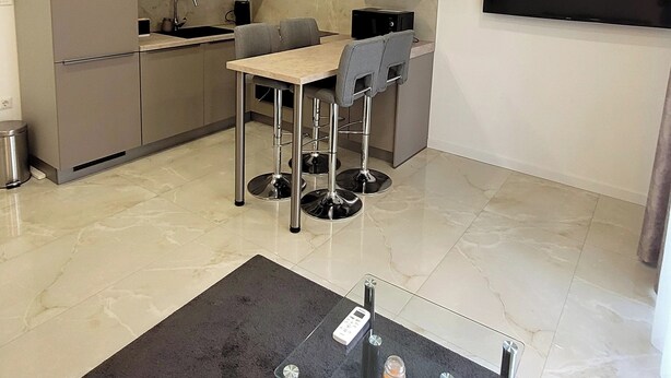 Een moderne keuken met een eethoek, een tv aan de muur en een kleine tafel met een glazen blad.