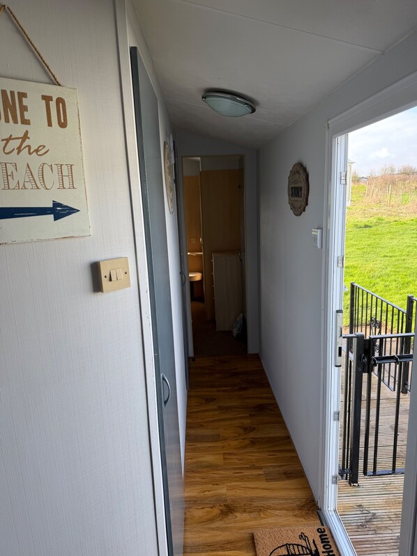 A hallway with a wooden floor leading to a room with a view of a grassy field. A sign on the wall reads "ONE TO THE BEACH". - Beautiful 3 Bed, Sleeps 6, Wifi, Pet Friendly (Bridlington)