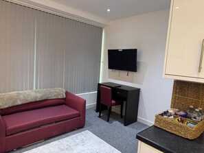 Un espacio habitable pequeño con un sofá, un escritorio, un televisor y un cesto de aperitivos.