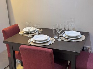 Mesa de comedor dispuesta con platos, vasos y cubiertos, rodeada de sillas rojas.
