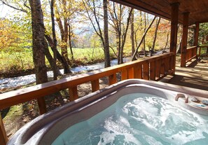 Un jacuzzi en una terraza de madera con vistas a un río y follaje otoñal.