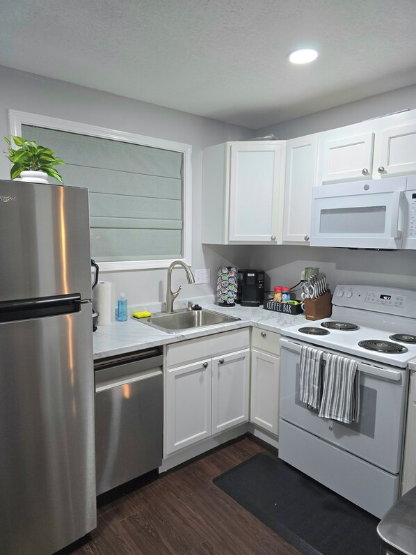 A modern kitchen with stainless steel appliances, white cabinetry, a built-in microwave, and a window with blinds.