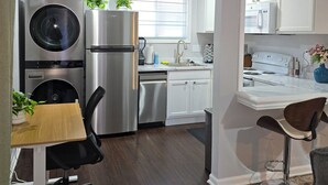 Een moderne keuken met roestvrijstalen apparatuur, een eethoek met een houten tafel, en een klein kantoongedeelte met een stoel.