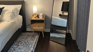Een netjes ingerichte slaapkamer met een bed, nachtkastje, lamp en een grote spiegel.
