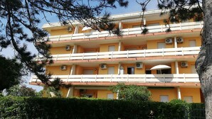 Un immeuble à plusieurs étages doté de balcons, de climatiseurs et d’une entrée sécurisée par un portail.