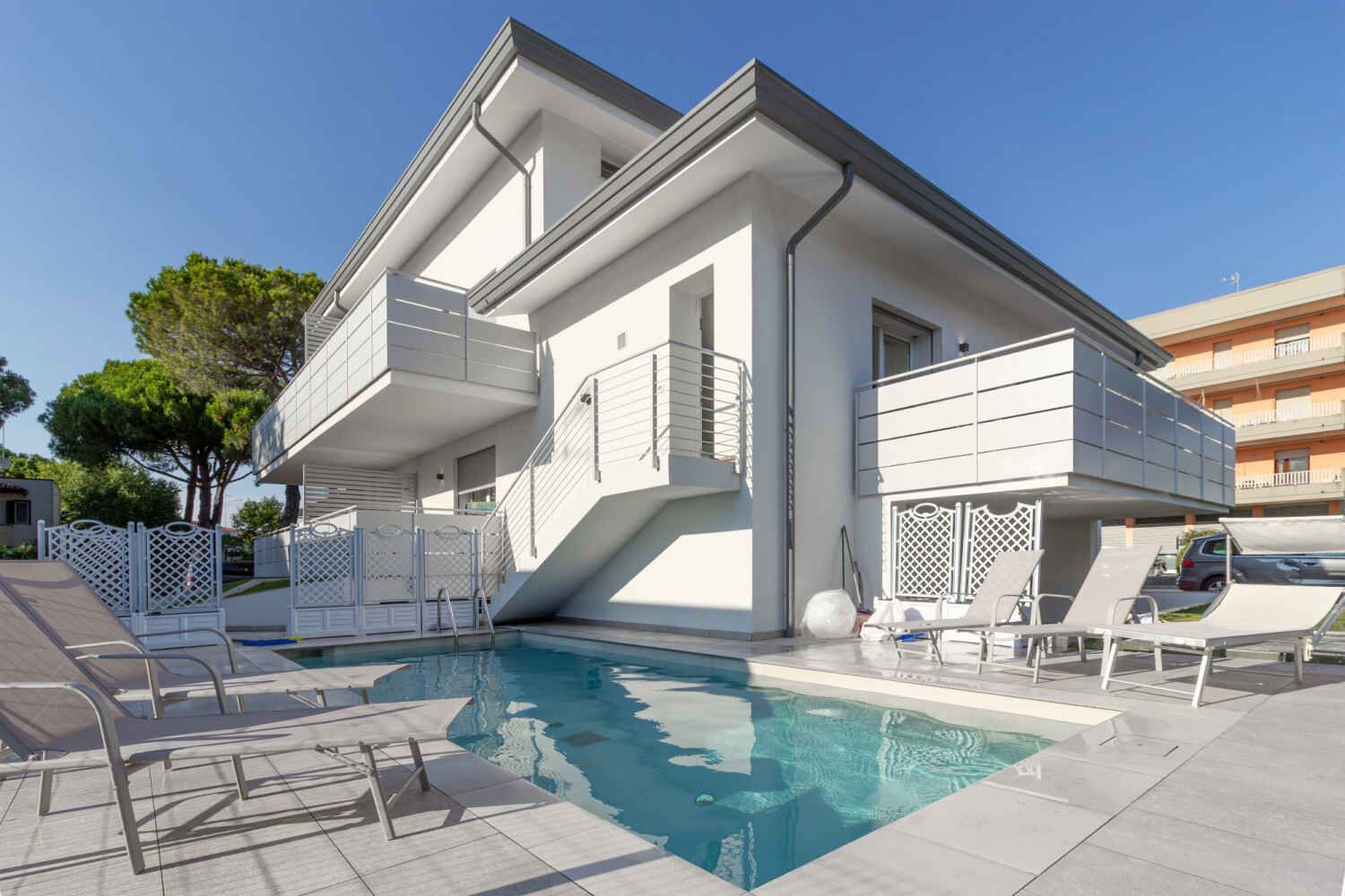 A modern two-story building with a swimming pool, outdoor seating, and a balcony.