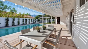 Eine Außenpatio mit Pool, weißem Pergola und Sitzbereich.