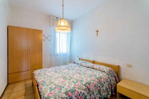 Ein Schlafzimmer mit einem Bett, einem Kleiderschrank, einer Hängelampe und einem Kruzifix an der Wand.
