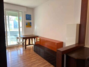 Ein Zimmer mit Holzboden, einem Schreibtisch mit Stuhl, einer Bank und einem Fernseher auf einem Standfuß.