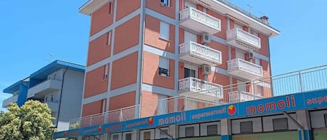 A multi-story building with a commercial ground floor featuring a supermarket named 'mobili' and a parking area with several cars.