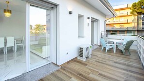 En moderne udendørs terrasse med spiseplads, skydedøre og en hvid facade.