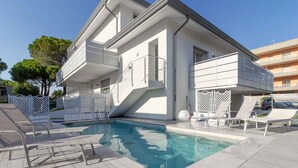 En modern tvåvåningsbyggnad med en swimmingpool, utomhusmöbler och en balkong.