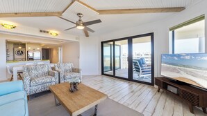 Uma sala de estar espaçosa com ventilador de teto, uma televisão grande e vista para a praia através de portas de correr.